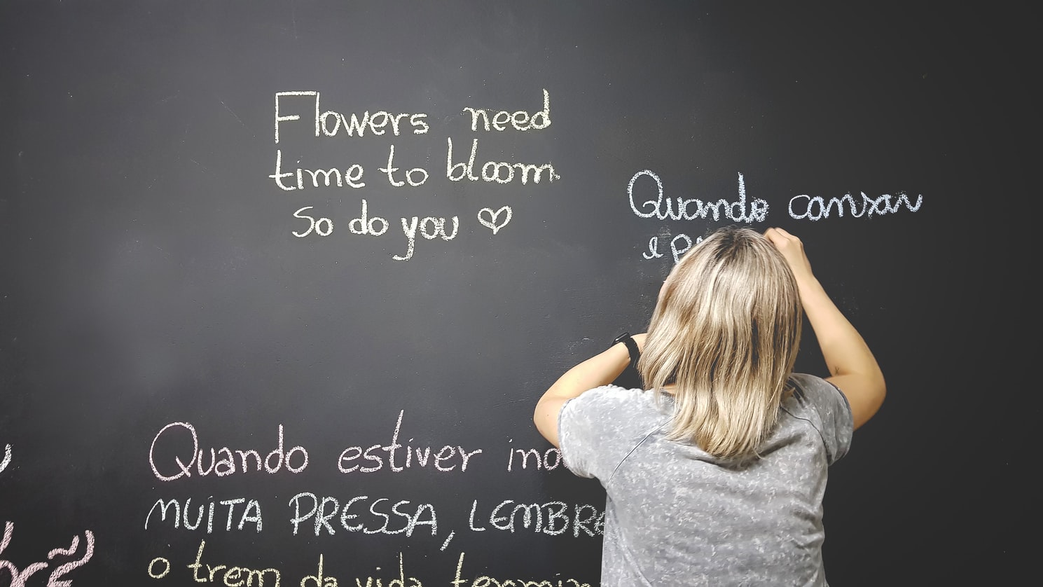 A blackboard with phrases written in different languages on it, and a child writing on it.